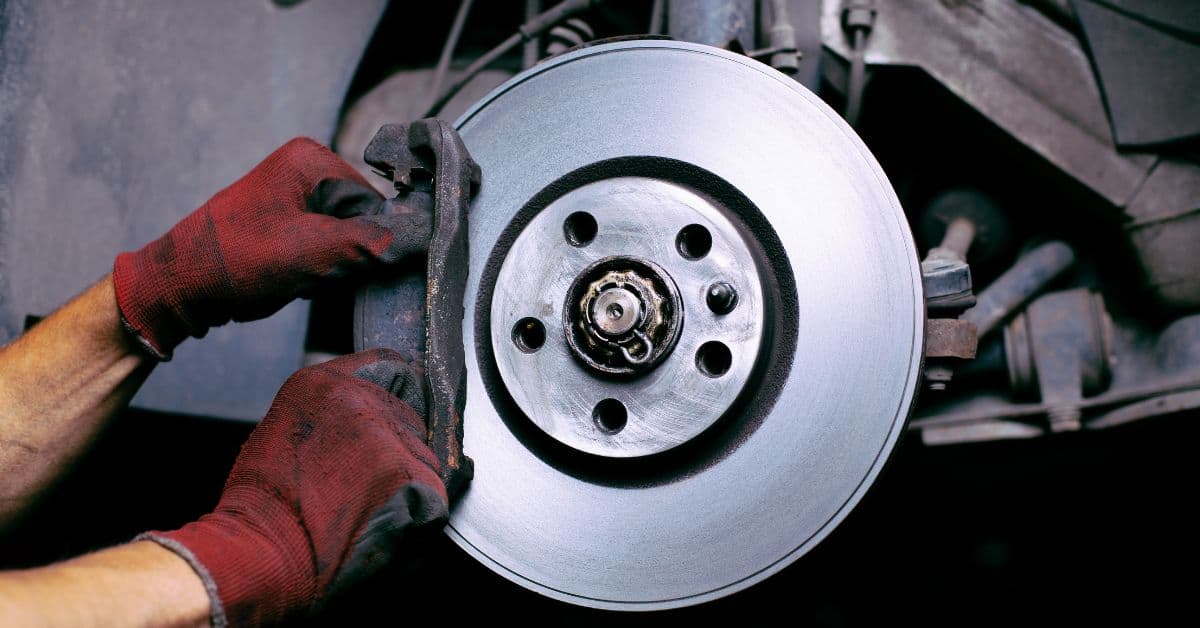 Gloved hands align brake pad against a metal brake rotor.