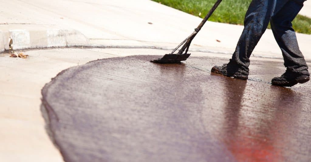 Person applying concrete resurfacer with a squeegee on driveway.