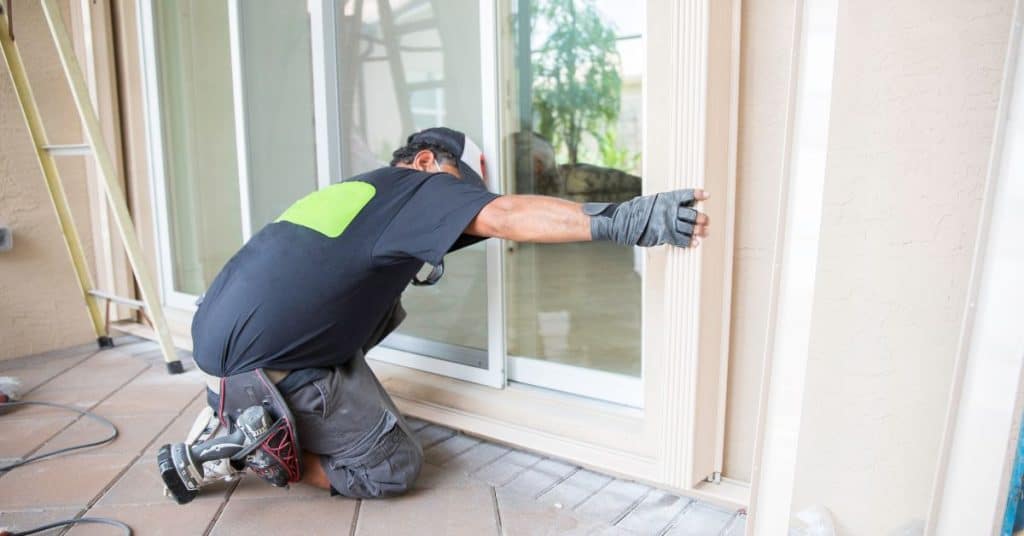 Technician kneels at sliding glass door, installing an impact-resistant hurricane window.