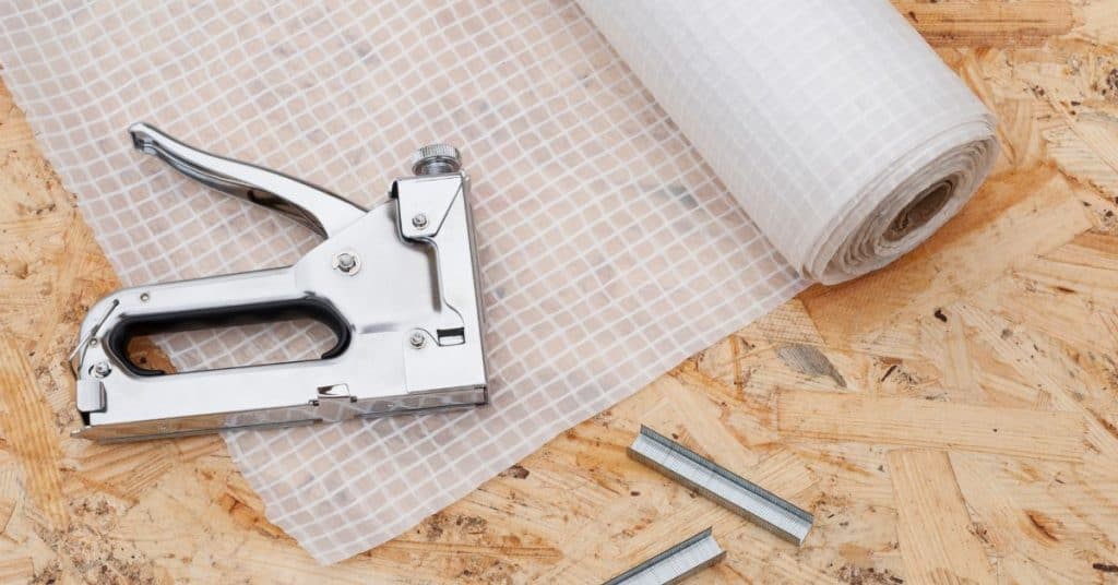 Staple gun beside roll of vapor barrier on plywood.