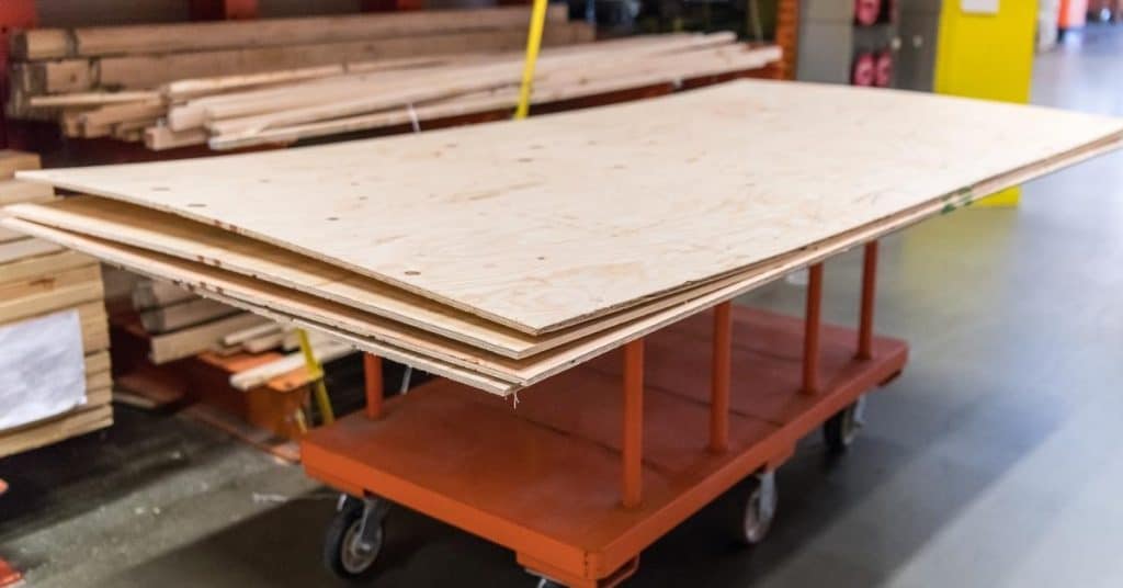 Plywood sheets stacked on an orange wheeled cart.
