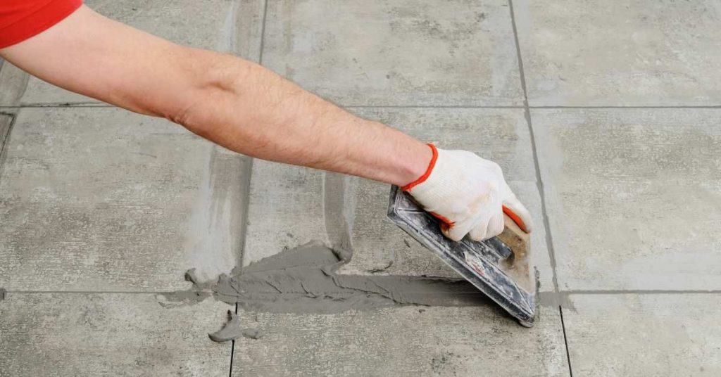 Smoothing gray grout into tile joints with a trowel.