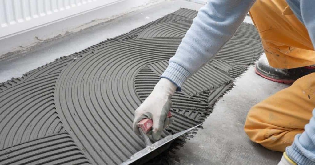 Person spreads thinset using a notched trowel, creating circular ridges.