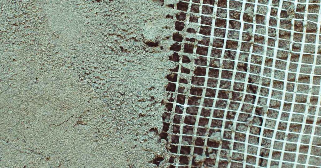 White mesh lath grid adjacent to cement-coated surface.