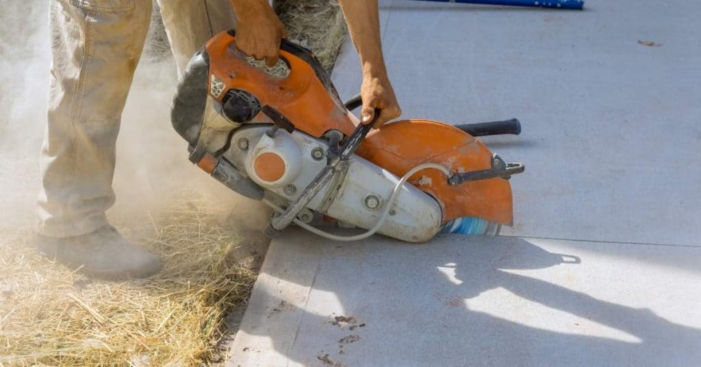 Worker using a concrete saw to cut a line in the driveway.