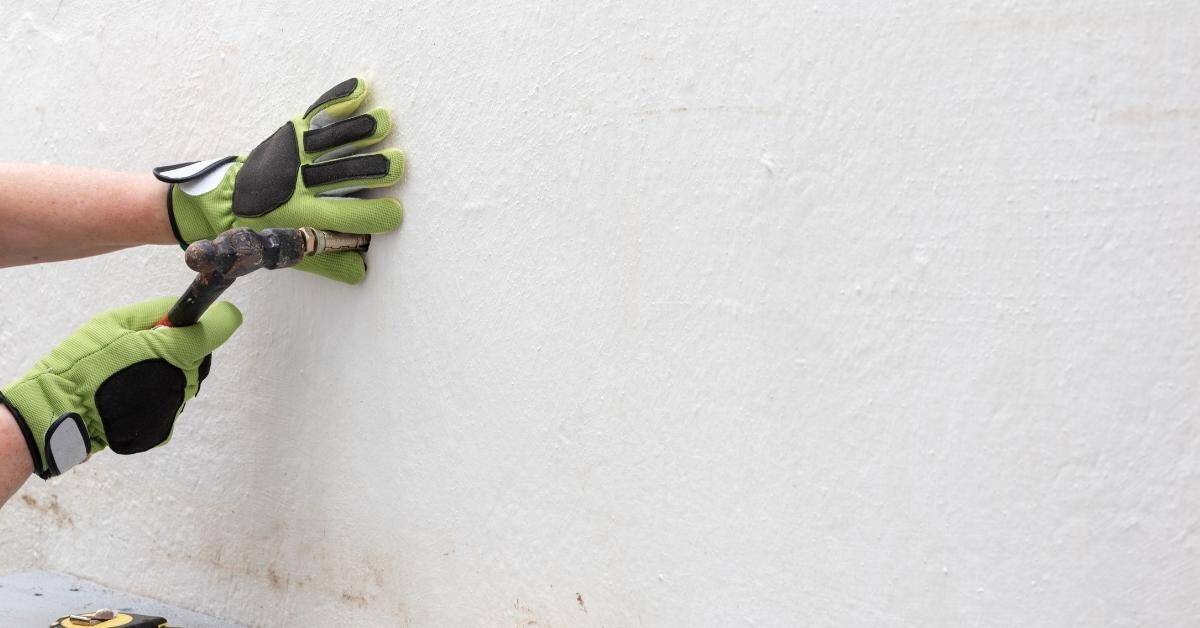 Gloved hands driving a metal anchor into concrete wall.