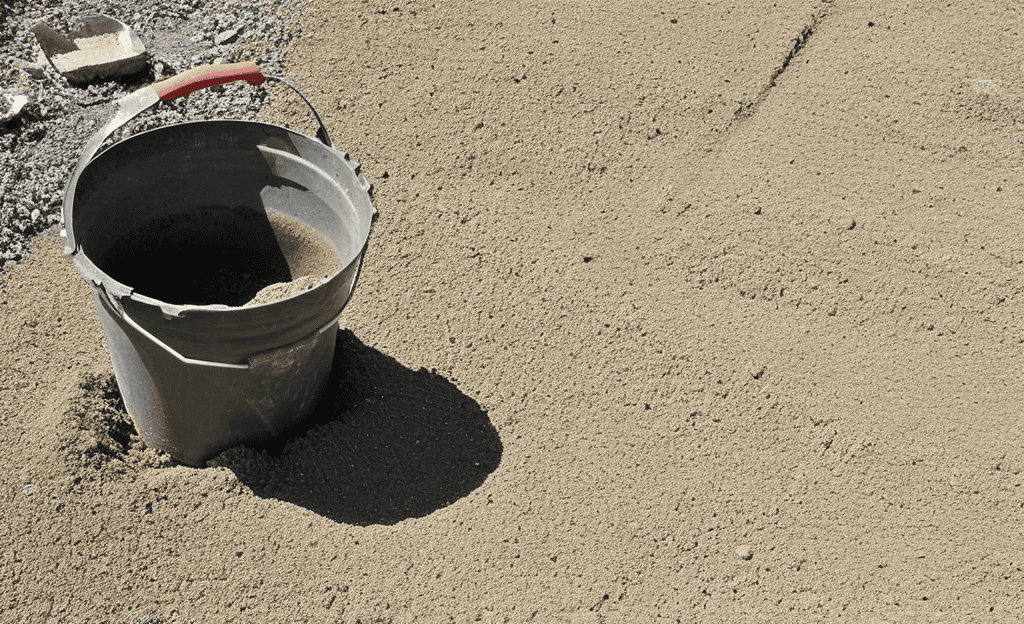 Plastic bucket partially buried in loose sand at site.