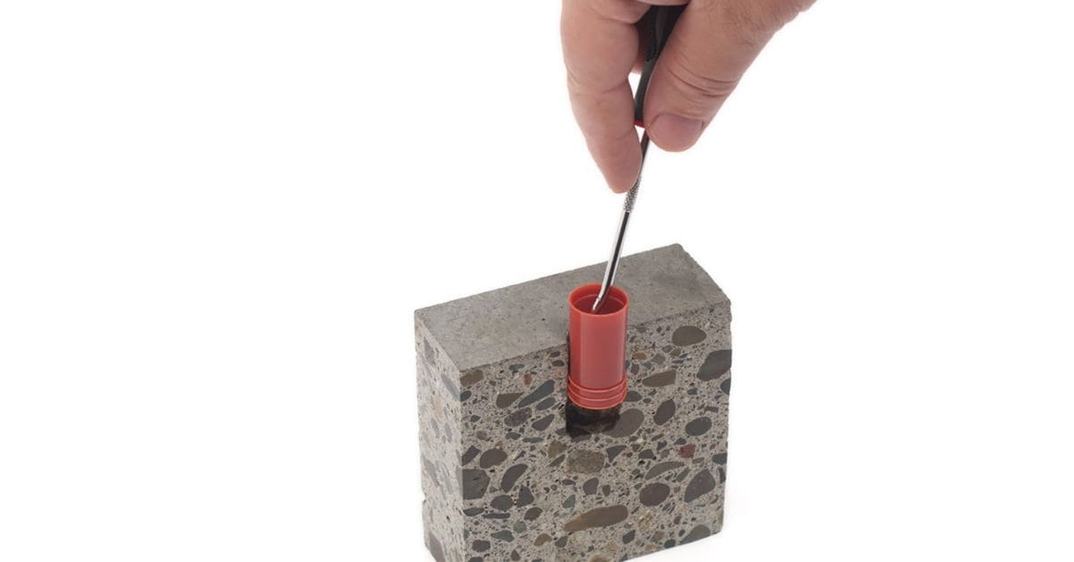Probe inserted into red plastic sleeve embedded in concrete block.