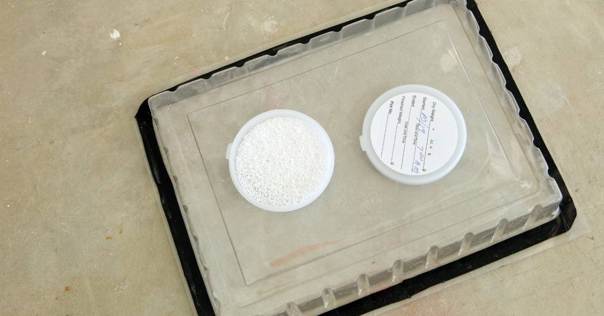 Two white bead containers on a moisture test tray over concrete.