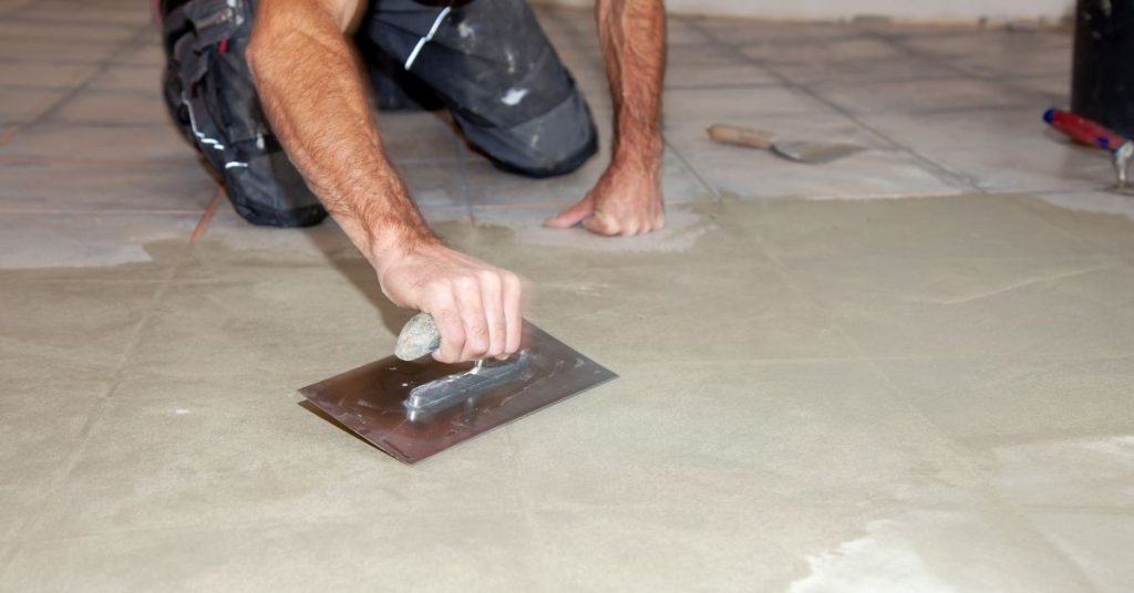 Trowel spreads leveling compound over floor during bathroom prep