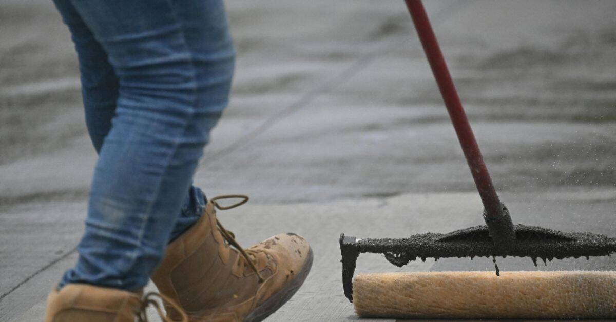 Roller applying dark sealant to stained concrete floor.
