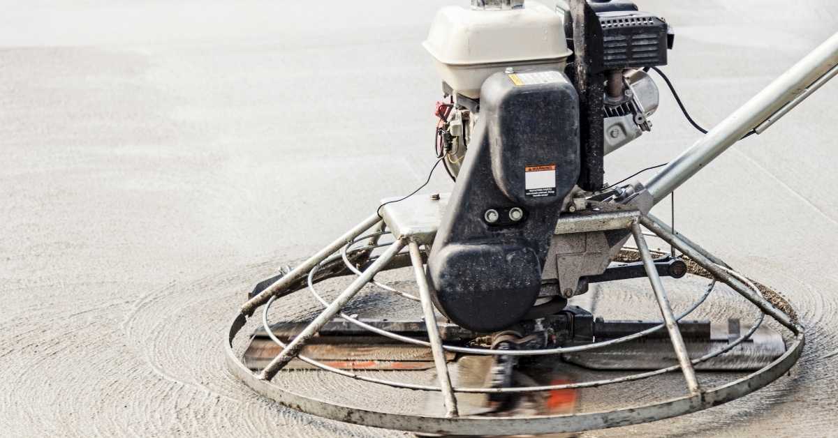 Gas-powered power trowel smoothing wet concrete with rotating blade ring.