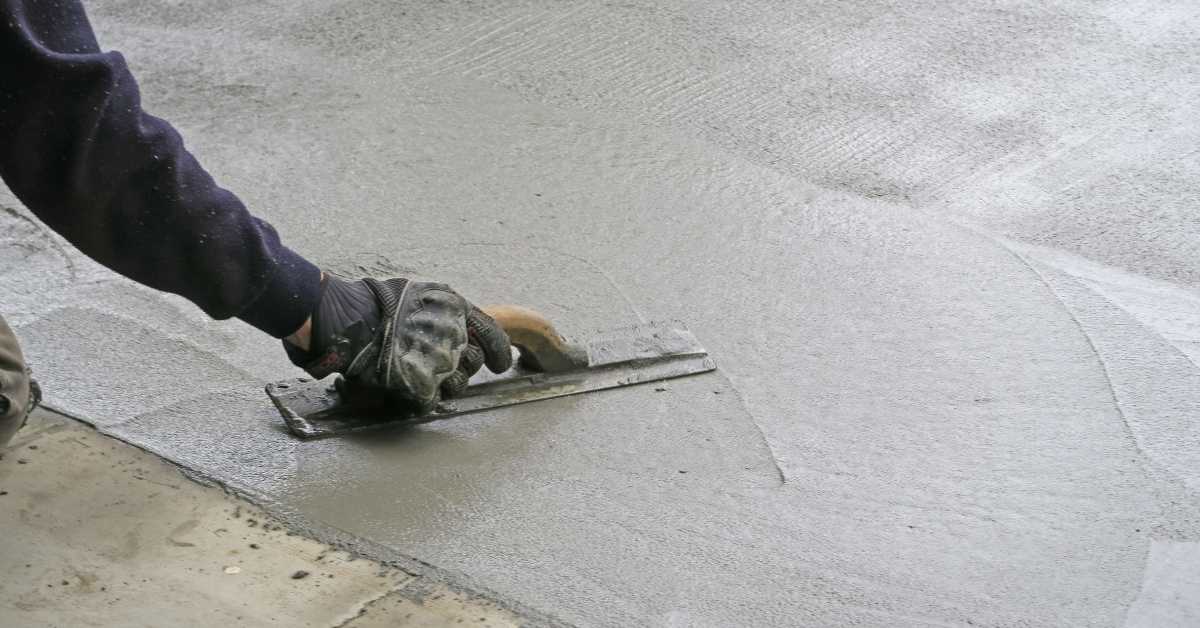 Gloved hand using a steel trowel to smooth concrete.