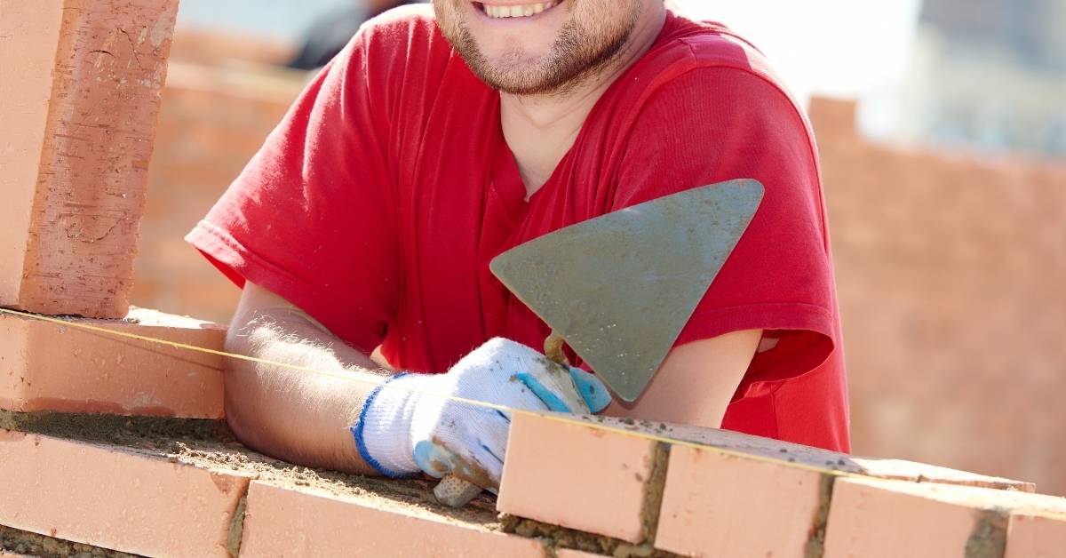Man in red shirt holding bricklaying trowel at brick wall