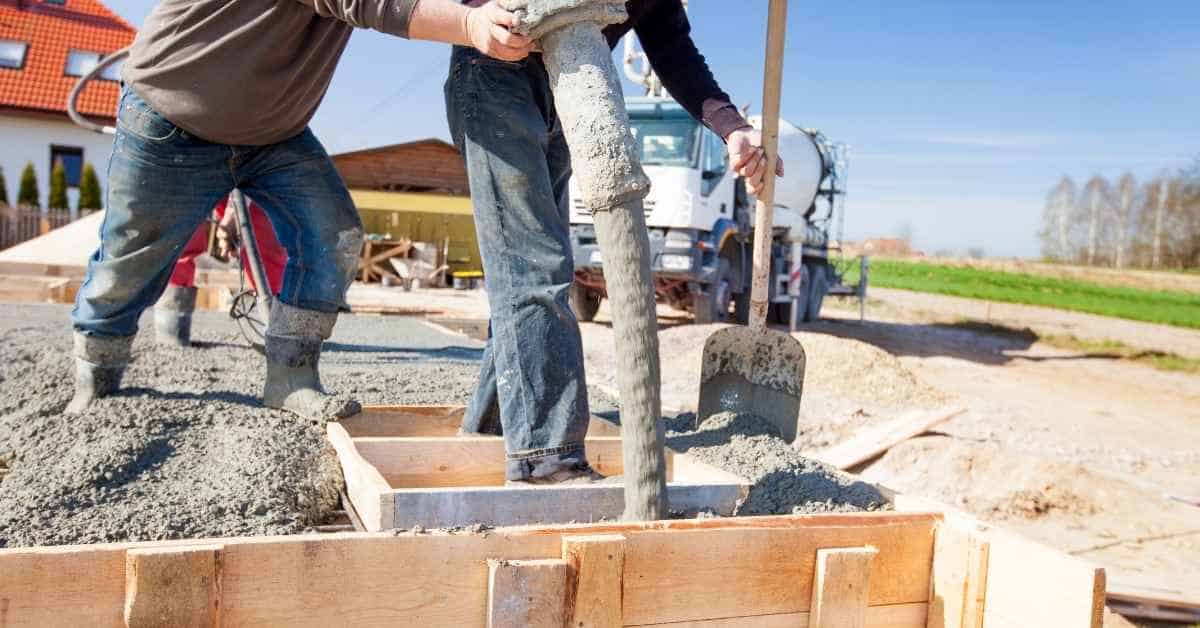 Workers pouring concrete into wooden formwork on sunny day