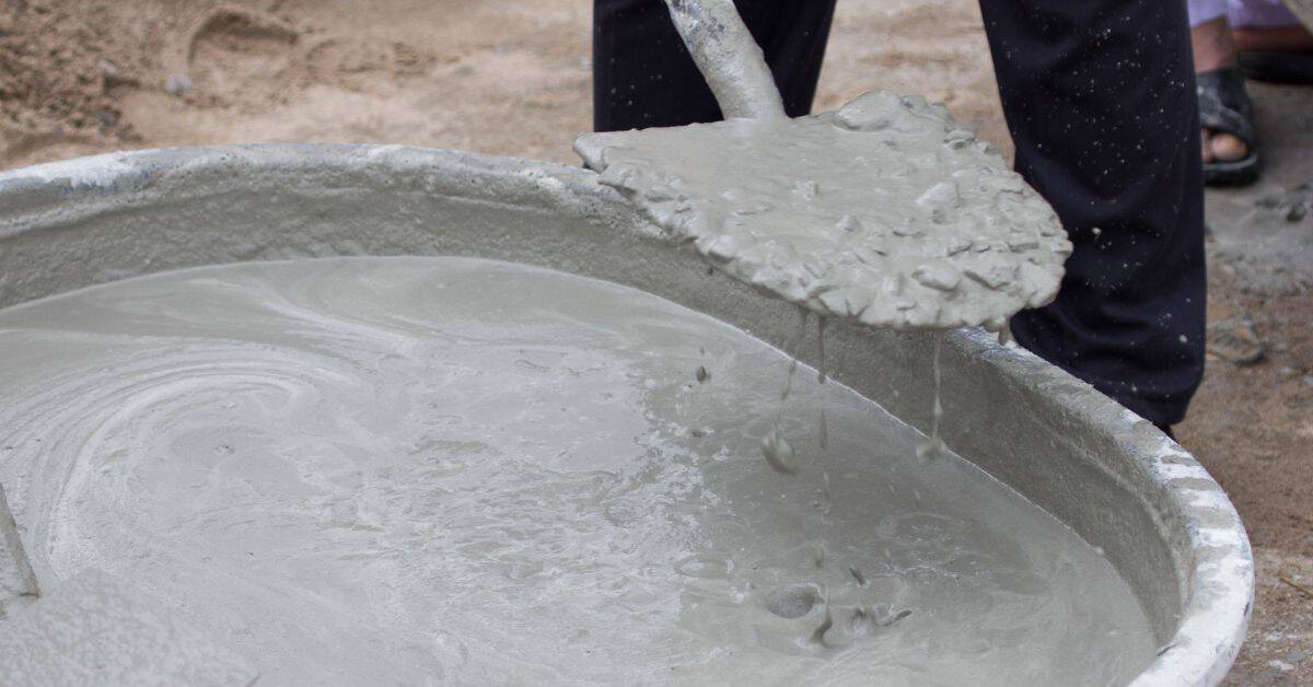 Wet concrete being mixed in a large basin with a shovel