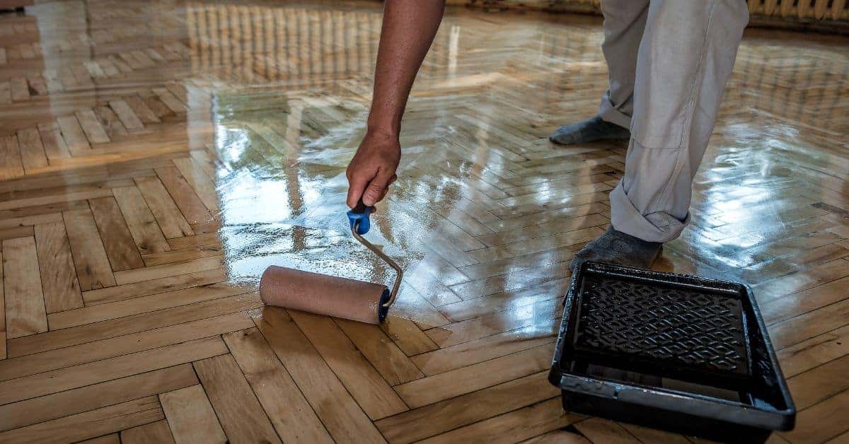 Person applying finish to wooden floor with paint roller