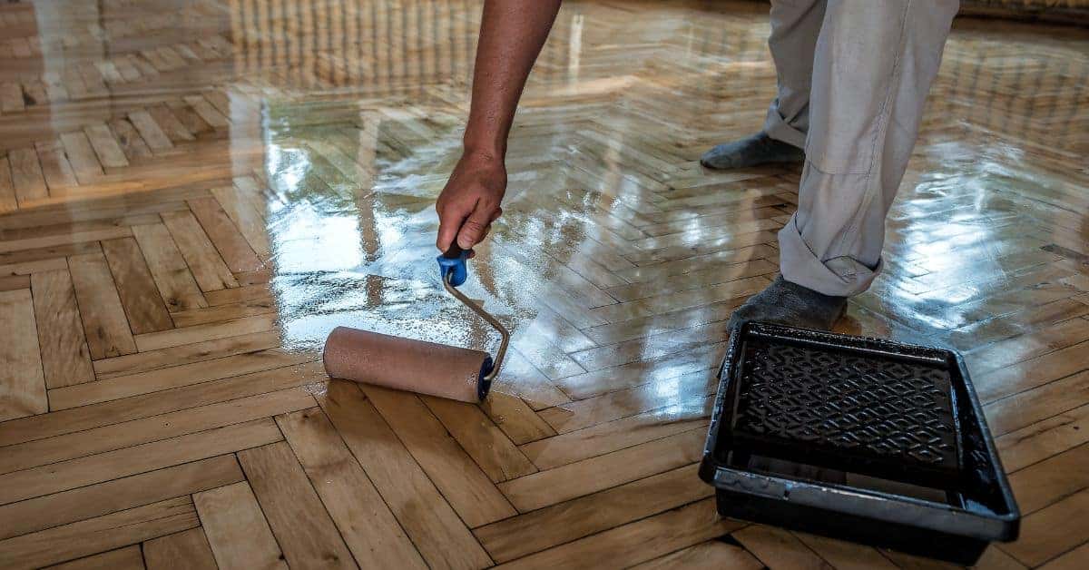 Person applying clear finish with roller on hardwood floor