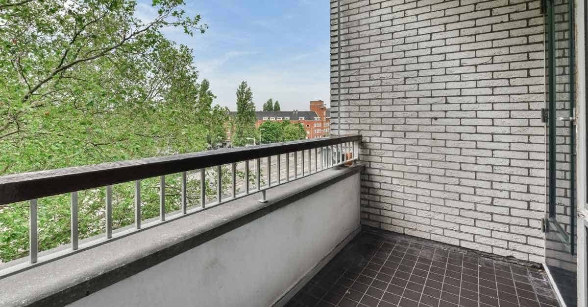 Balcony with tile flooring and railing overlooking trees and buildings