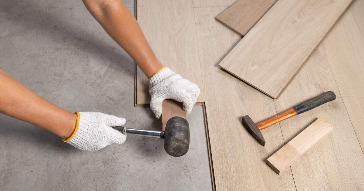 Person installing laminate flooring with mallet and tapping block