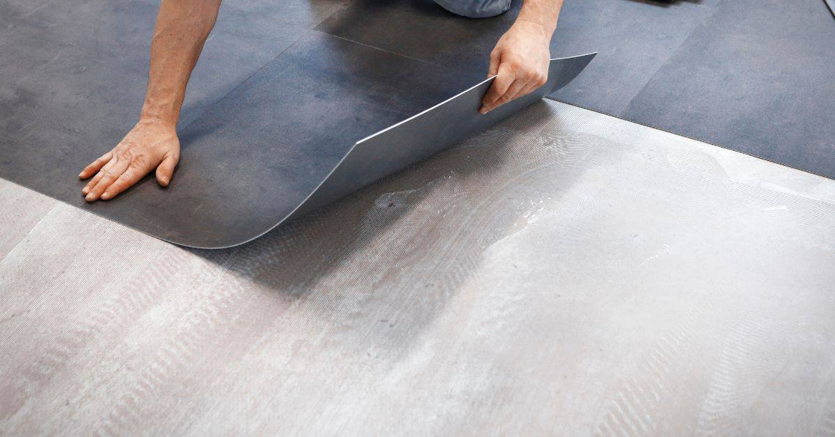 Person laying dark vinyl flooring sheet on subfloor