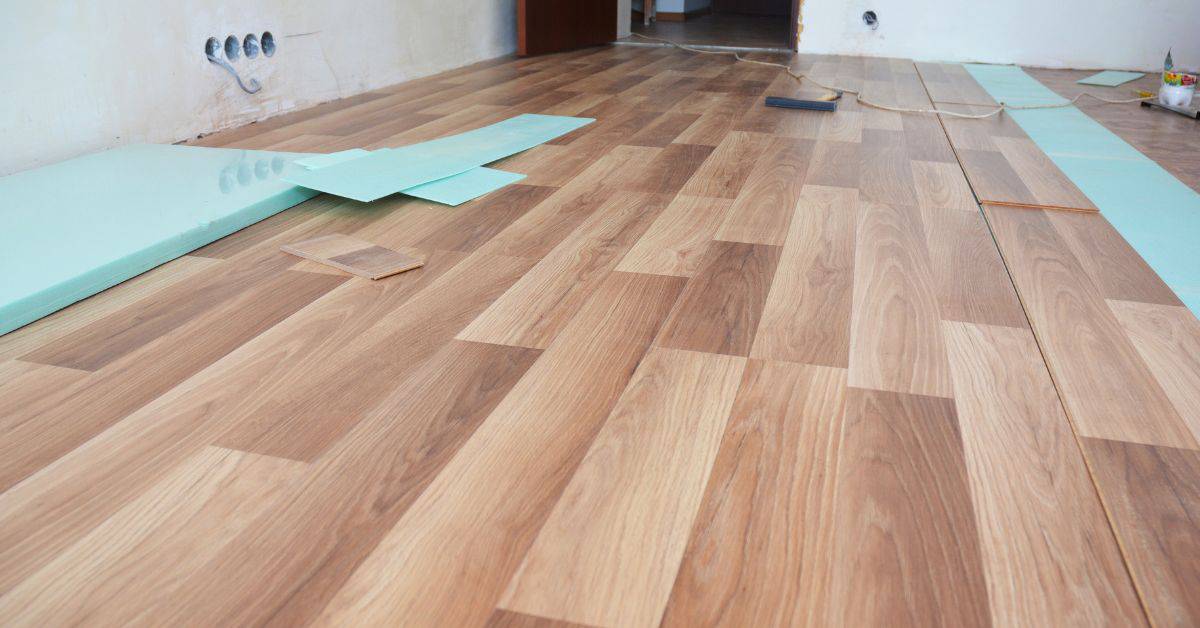wood laminate floor partially installed with green underlayment sheets