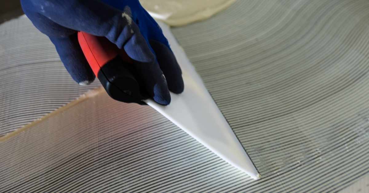 Hand wearing blue glove holds red notched trowel spreading adhesive