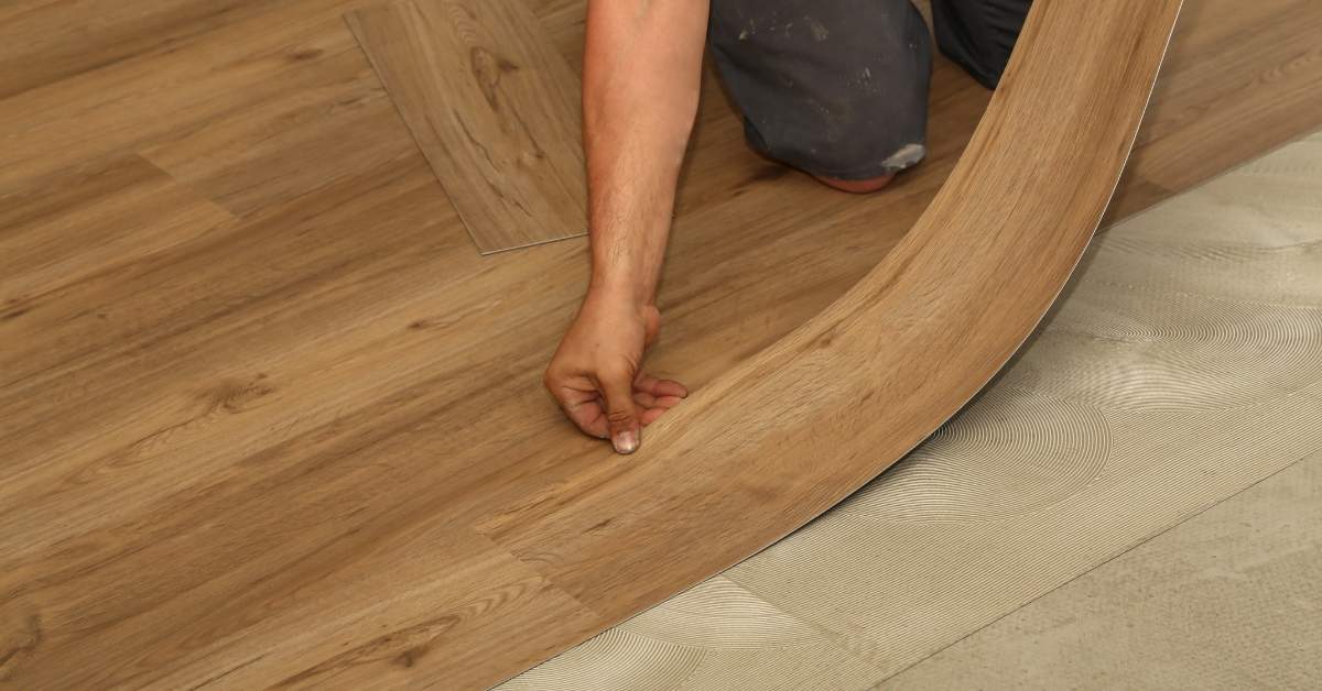Person laying flexible vinyl wood-look flooring over adhesive