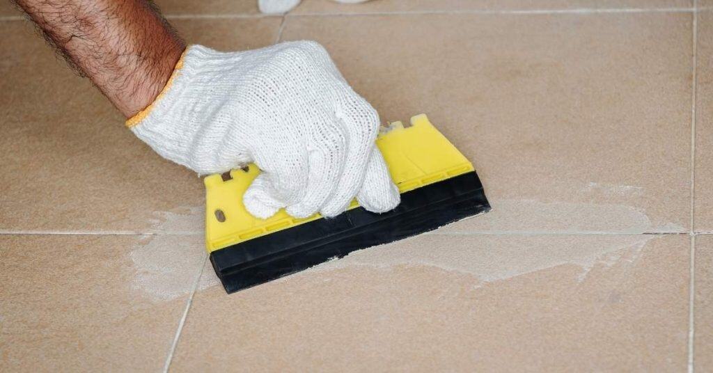 Hand with white glove spreading grout on floor tiles