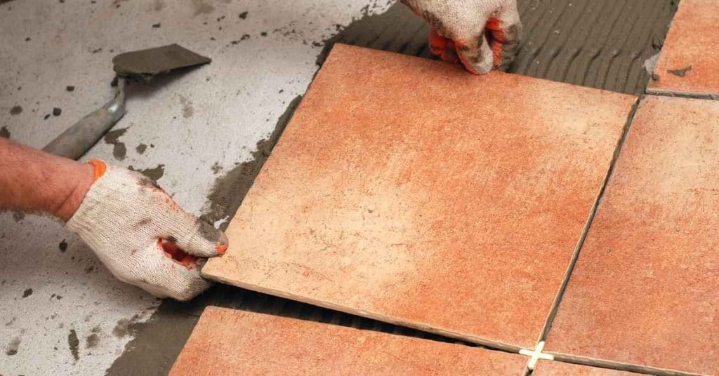 Hands installing square reddish ceramic floor tiles