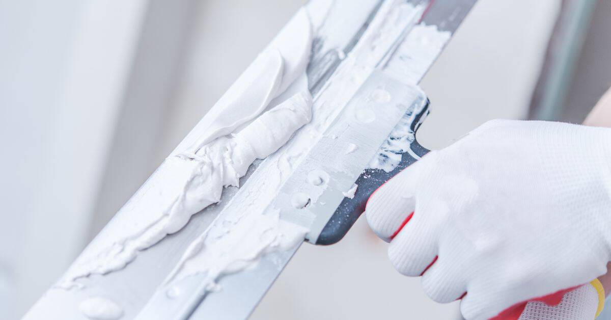 Hand in glove smoothing white caulk on window frame