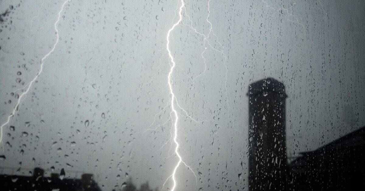 Lightning storm visible through rain-covered window with chimney silhouette