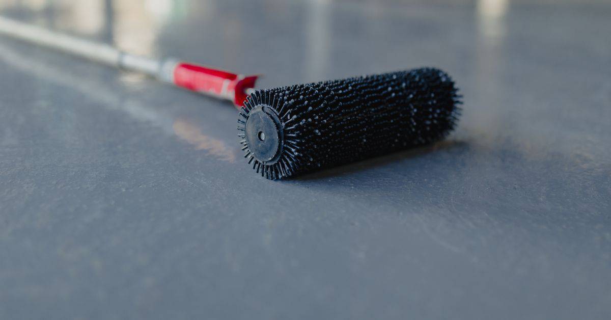 Black spiked roller with red handle on smooth concrete surface