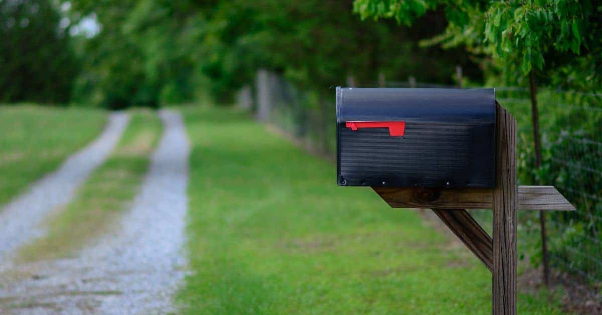 Black mailbox on wooden post near gravel driveway