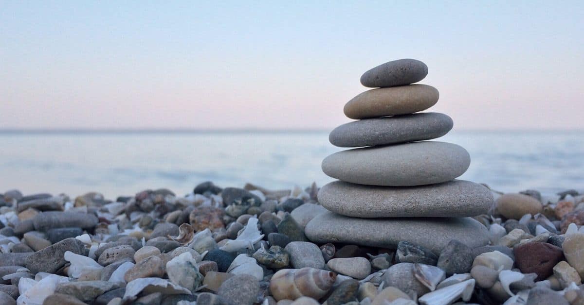 Stacked smooth stones on pebble-covered shore with water background