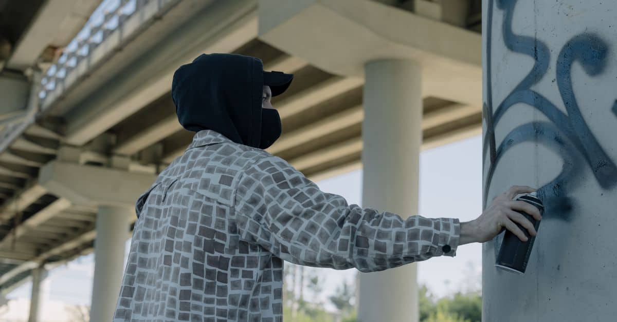 Person spraying black graffiti on concrete pillar outdoors