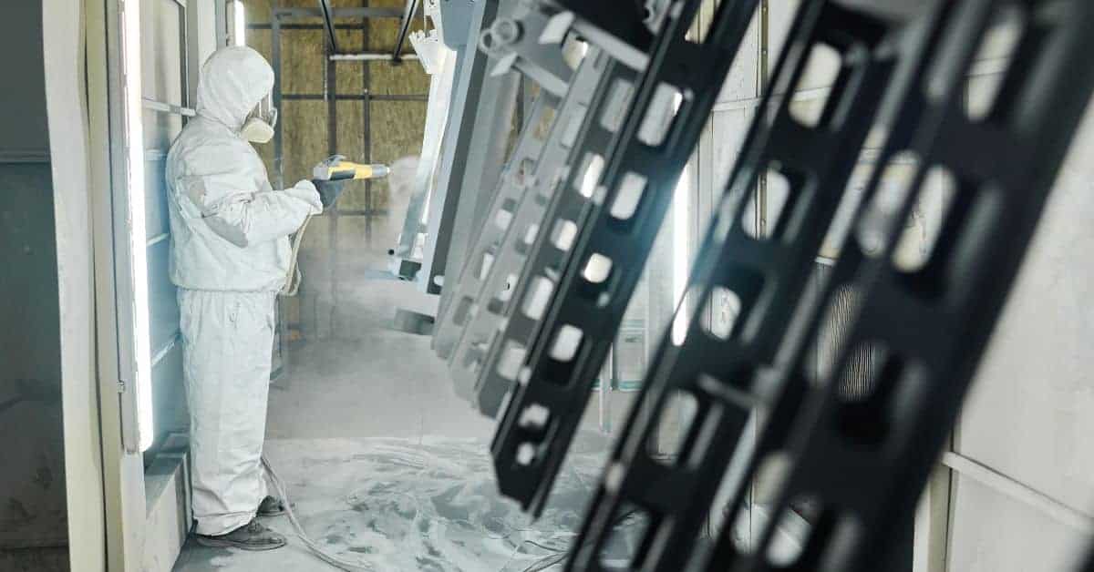 Person in protective suit spraying powder coating onto metal frames