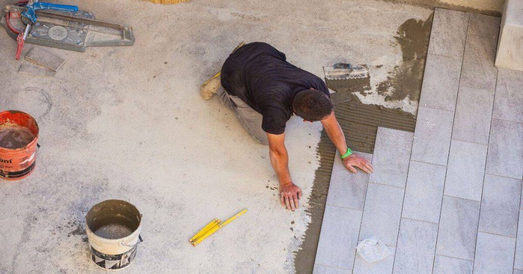 Man kneeling installing rectangular floor tiles