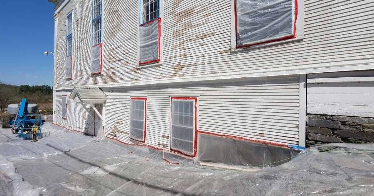 Exterior house wall with plastic sheets covering windows and ground