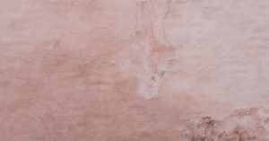 Faded pink stucco wall with visible cracks and repairs