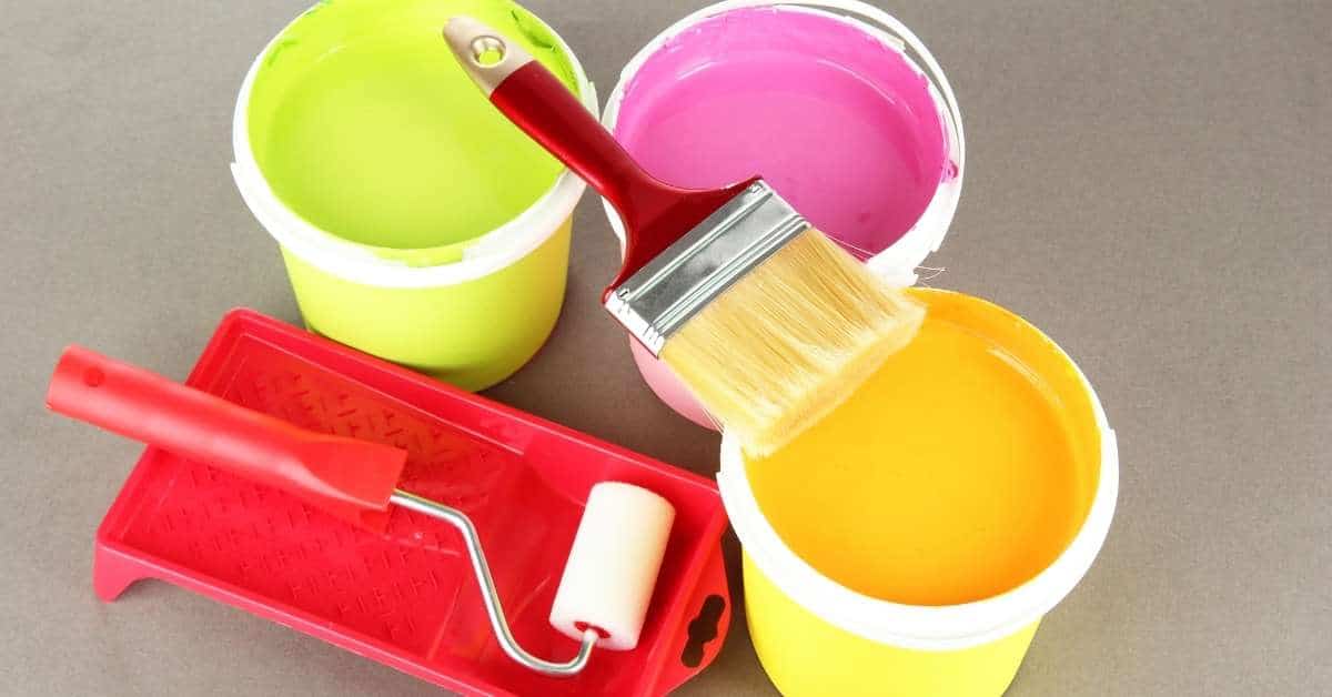 Open paint buckets with yellow, green, and pink paint and brushes