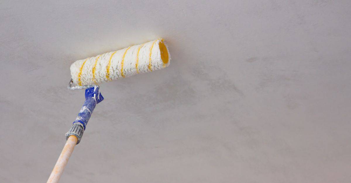 Paint roller applying gray paint to ceiling