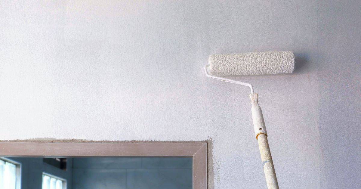 Paint roller applying white paint on wall near window frame