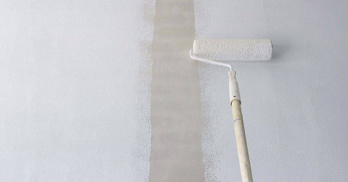 Paint roller applying light gray paint on white wall