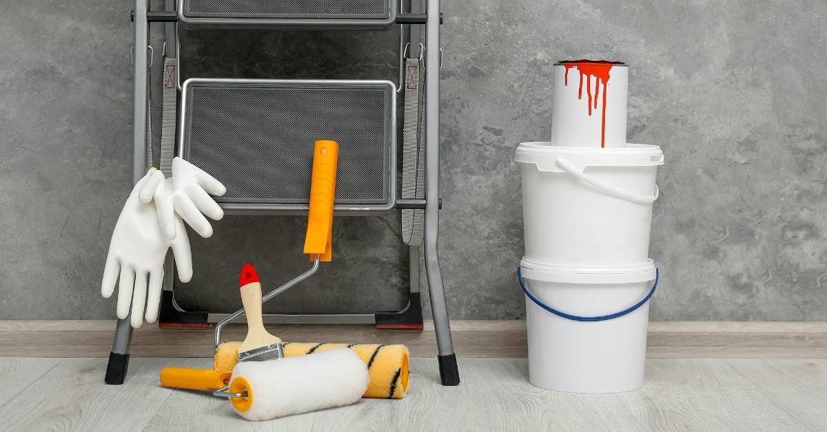 Paint rollers gloves brush stacked buckets gray wall