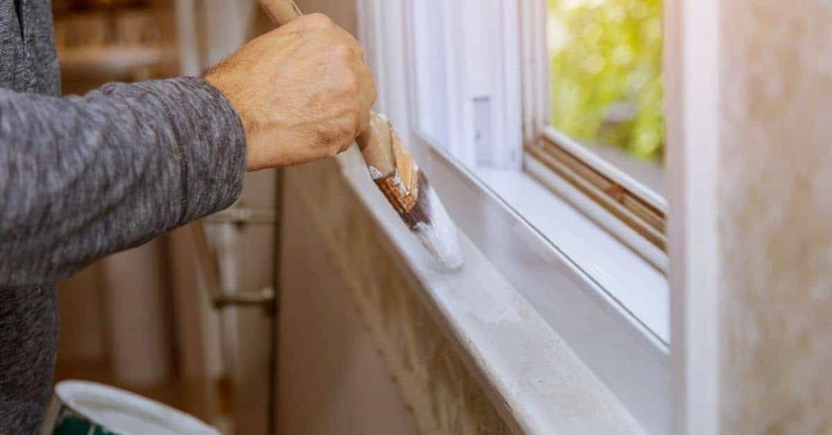 Person painting white window sill with brush
