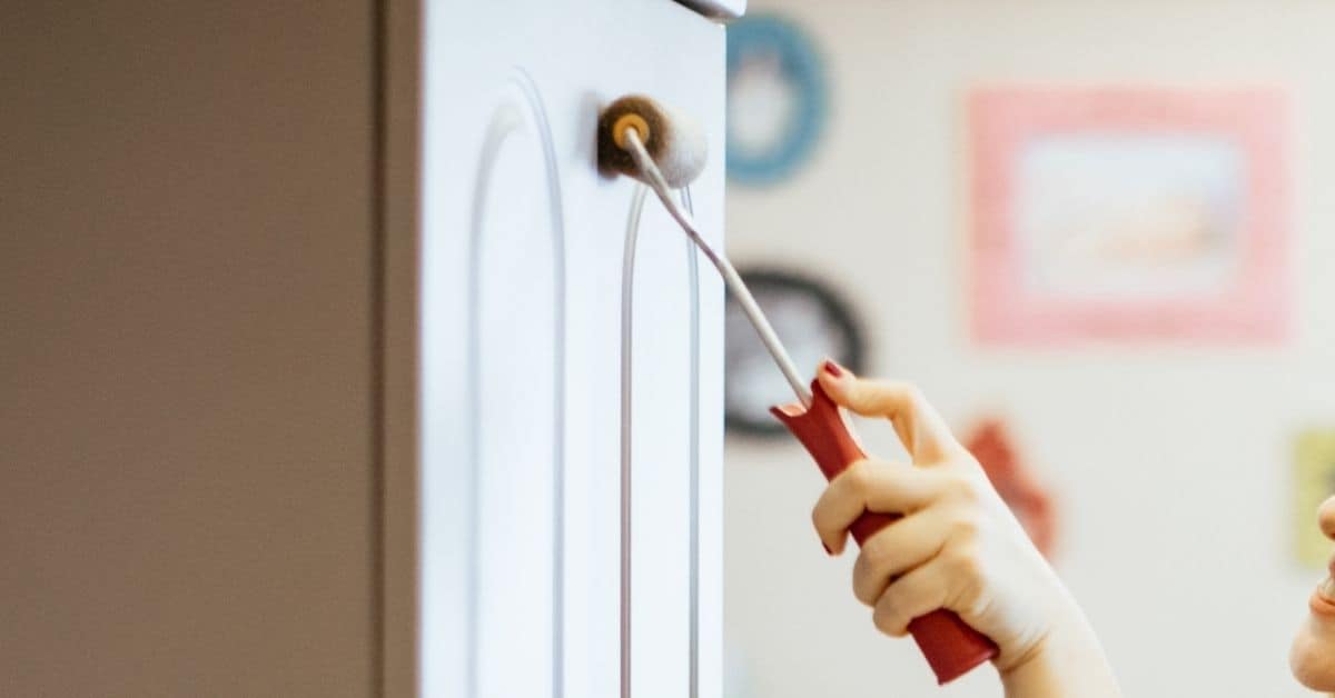 Hand using small paint roller on white cabinet door