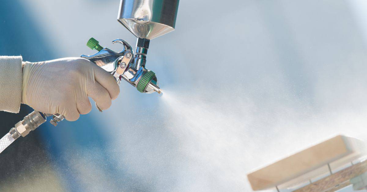 Hand with glove spraying coating with spray gun