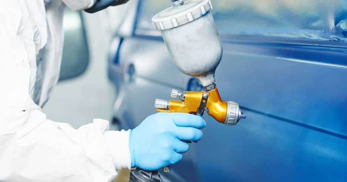 Person spray painting blue car panel wearing protective gloves