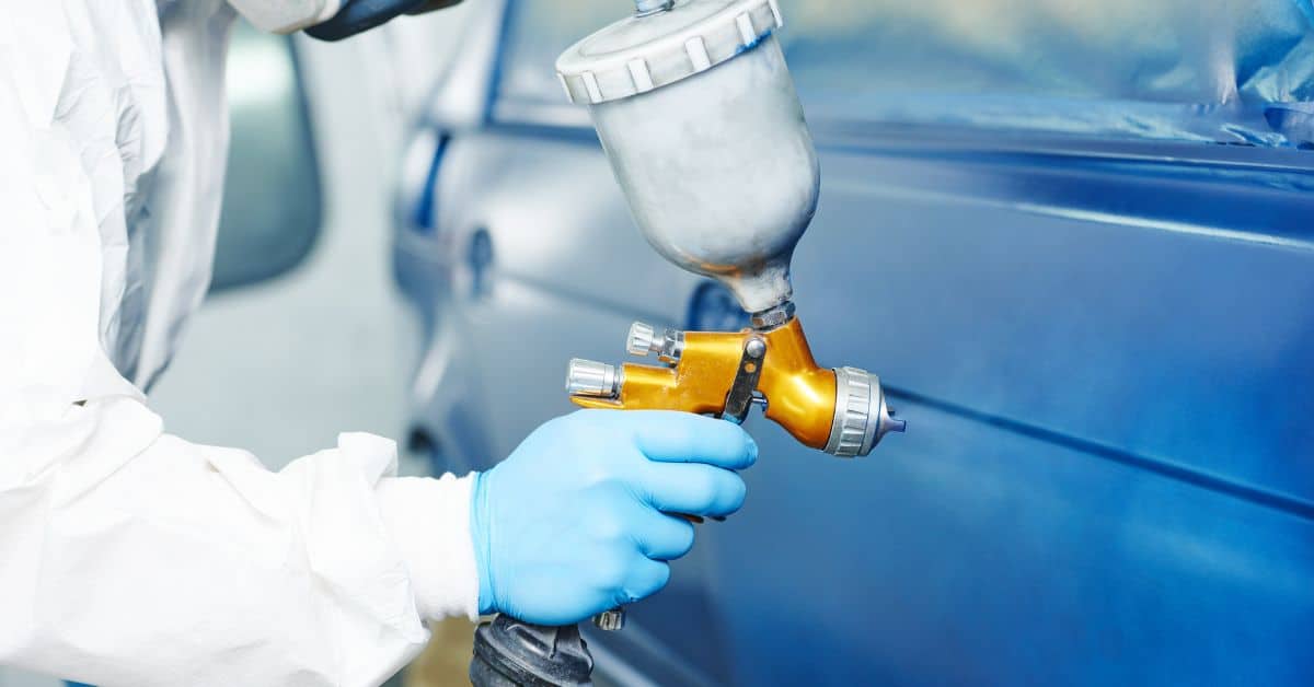 Person spray painting blue car door wearing protective gloves